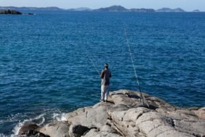 liberacao da pesca: pessoa pescando em um costão rochoso diante de um mar azul.