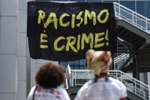 igualdade racial: Duas pessoas observam faixa preta com a frase "Racismo é crime!" em evento em Brasília.
