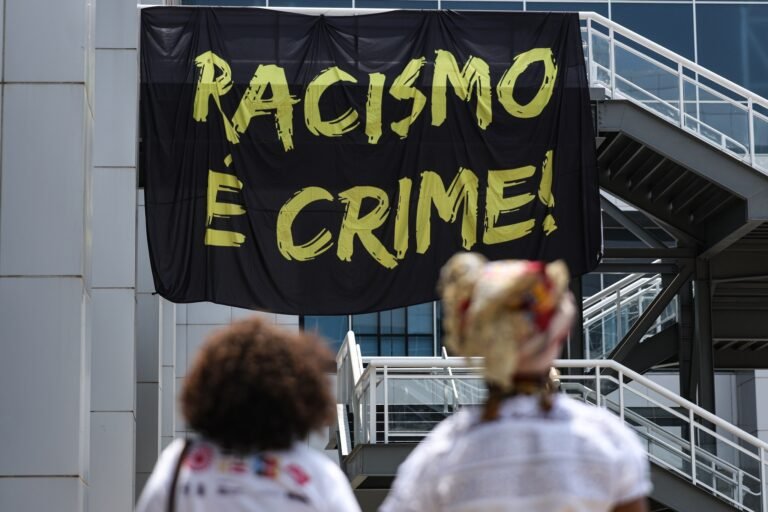 Consulta pública sobre políticas de igualdade racial termina hoje 5 igualdade racial: Duas pessoas observam faixa preta com a frase "Racismo é crime!" em evento em Brasília.