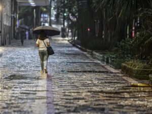 chuvas fortes: mulher de costas caminha sob um guarda-chuva preto em calçada de pedras molhada pela chuva.