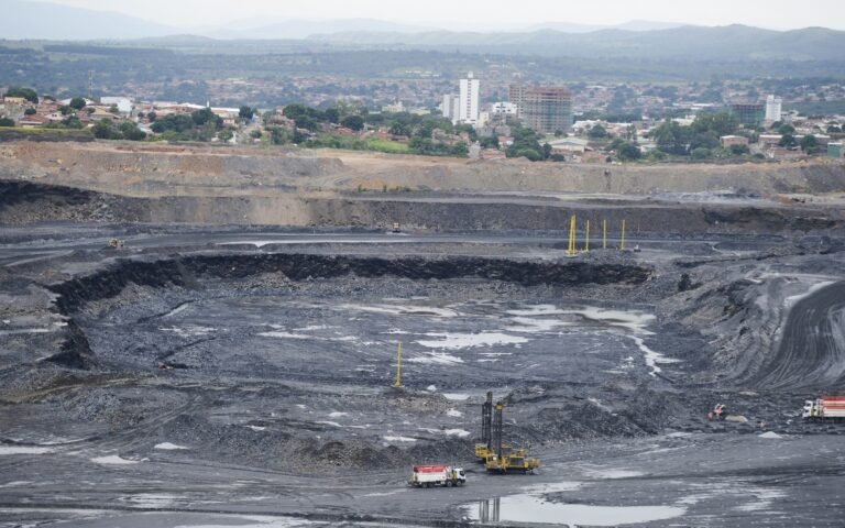 minerais criticos: vista panorâmica de uma mina a céu aberto com maquinários pesados e área urbana ao fundo.