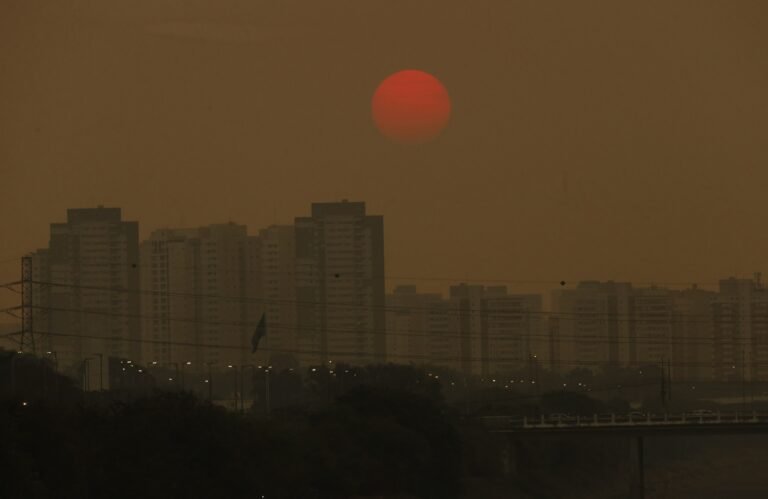 Emissão líquida de poluentes no país cai ao menor nível desde 2012 6 meta climatica: Prédios de São Paulo sob céu amarronzado por poluição com sol vermelho ao fundo.