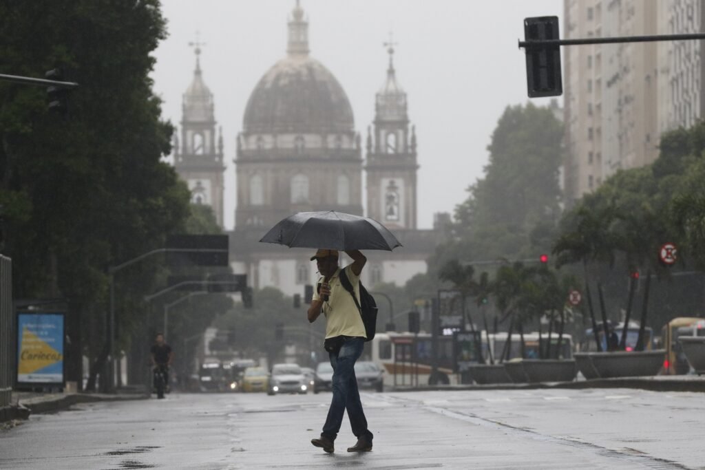 tempestades: Homem caminha sob guarda-chuva em rua molhada durante temporal.