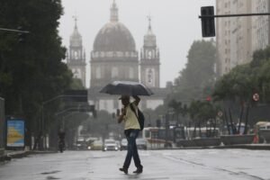 tempestades: Homem caminha sob guarda-chuva em rua molhada durante temporal.