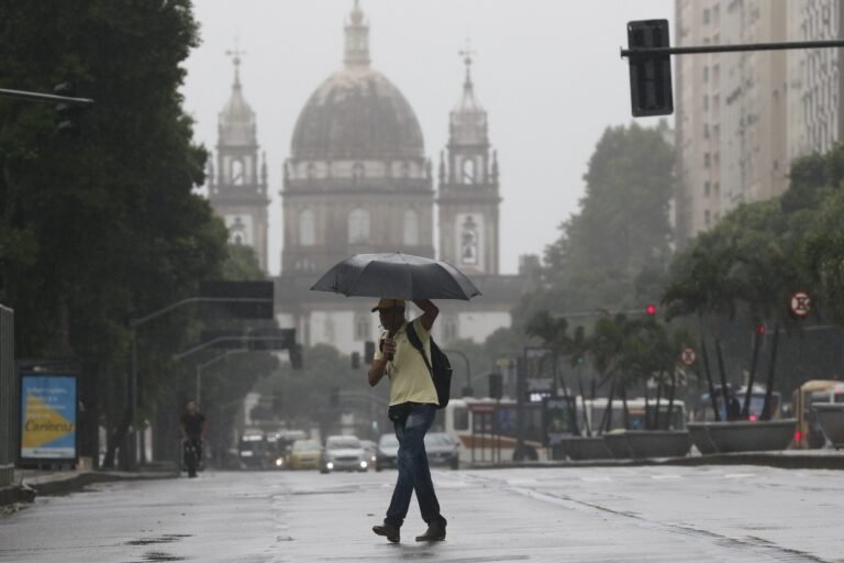 Frente fria leva tempestades e granizo ao centro-sul do país 4 tempestades: Homem caminha sob guarda-chuva em rua molhada durante temporal.