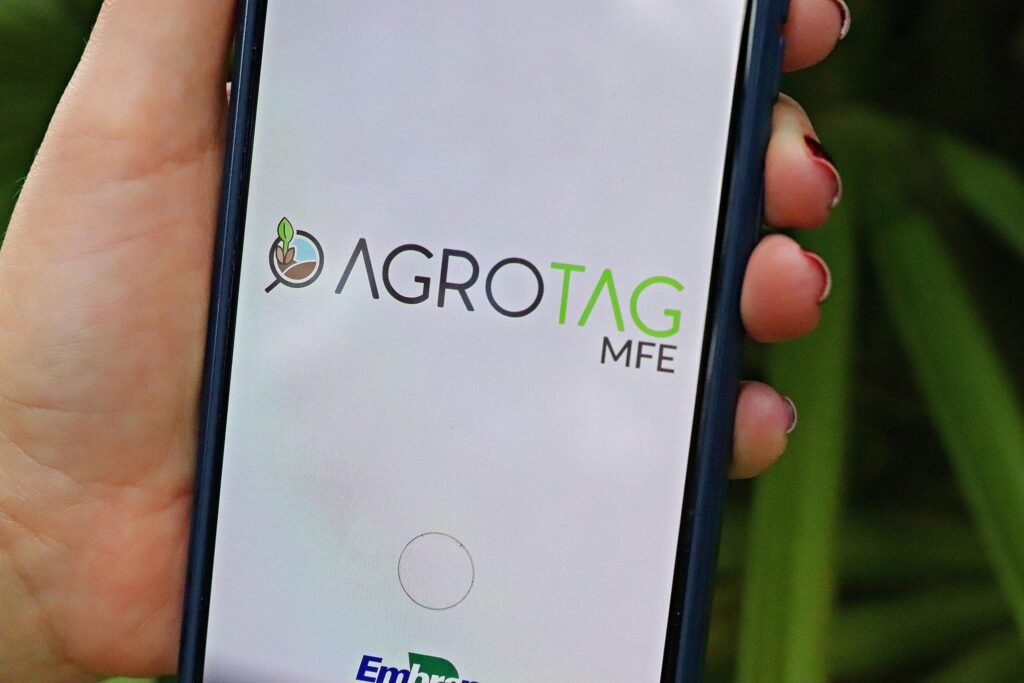 efeito estufa: Mão segurando smartphone com o logotipo Agrotag MFE da Embrapa.