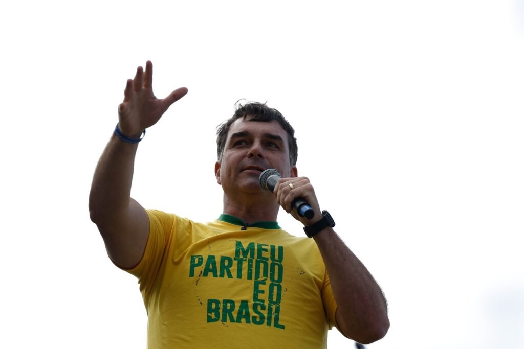 agendas de campanha: Flávio Bolsonaro discursa ao microfone com a mão erguida em evento político.