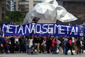 Manifestantes seguram faixa com os dizeres "META, NÃO SE META!" em protesto na rua.