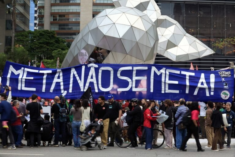 Manifestantes seguram faixa com os dizeres "META, NÃO SE META!" em protesto na rua.